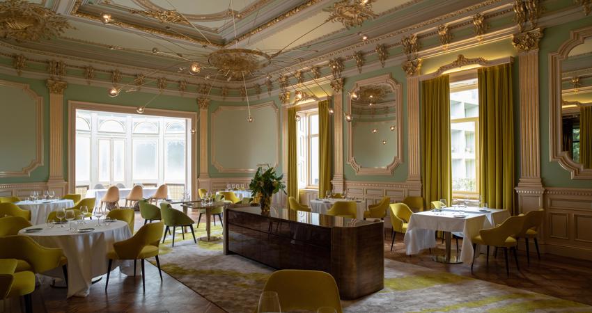 El salón del restaurante mezcla un estilo historicista con enfoques modernos siguiendo una gama de color entre amarillos y verdes