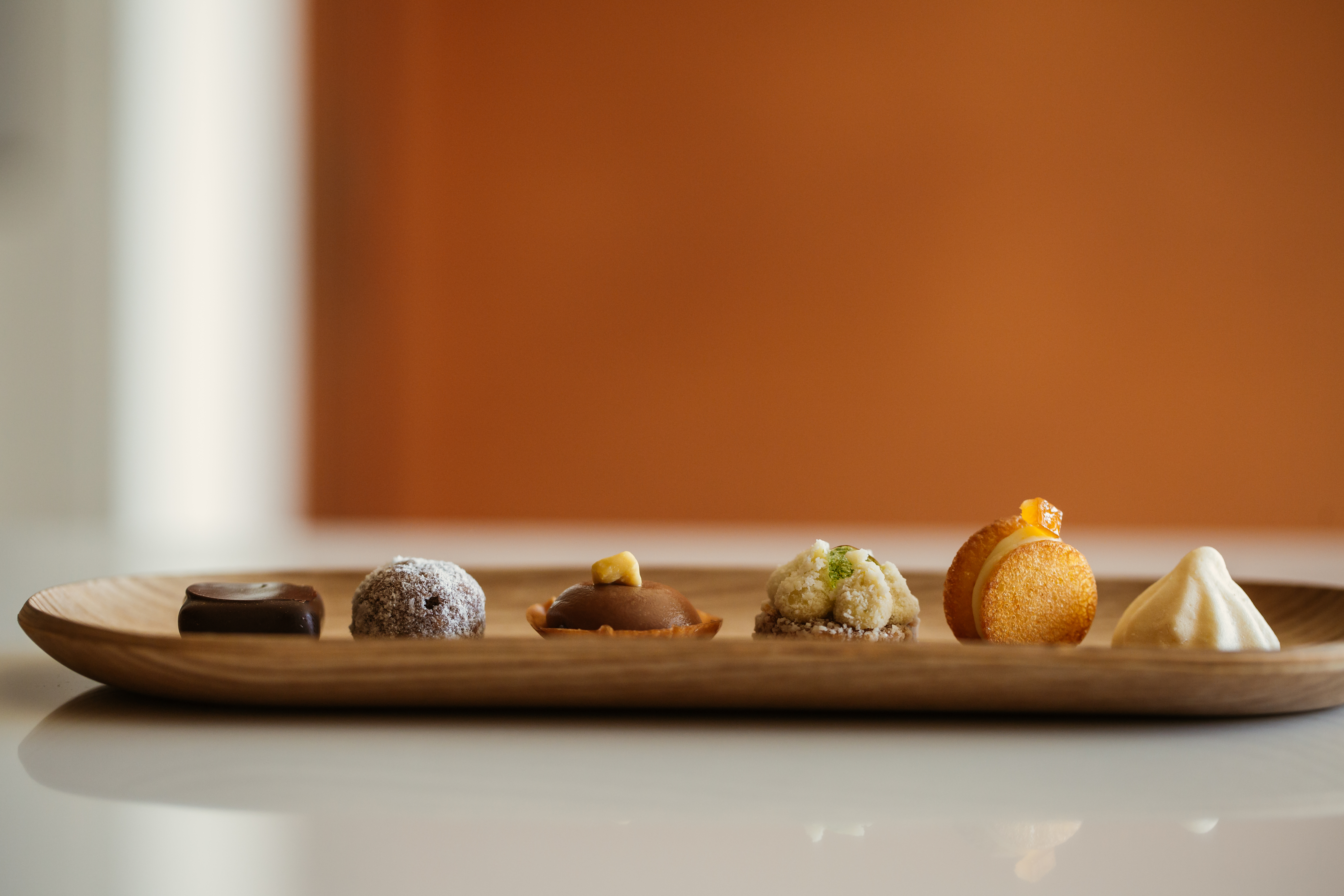 Presentation of one of La Gaia's passes, with small sweet morsels on a light wooden plate