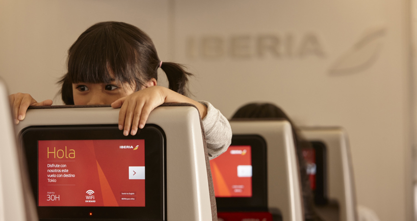 Beneficios de Iberia Plus Kids. En la imagen, una niña se asoma por encima de uno de los asientos de un avión de largo radio de Iberia