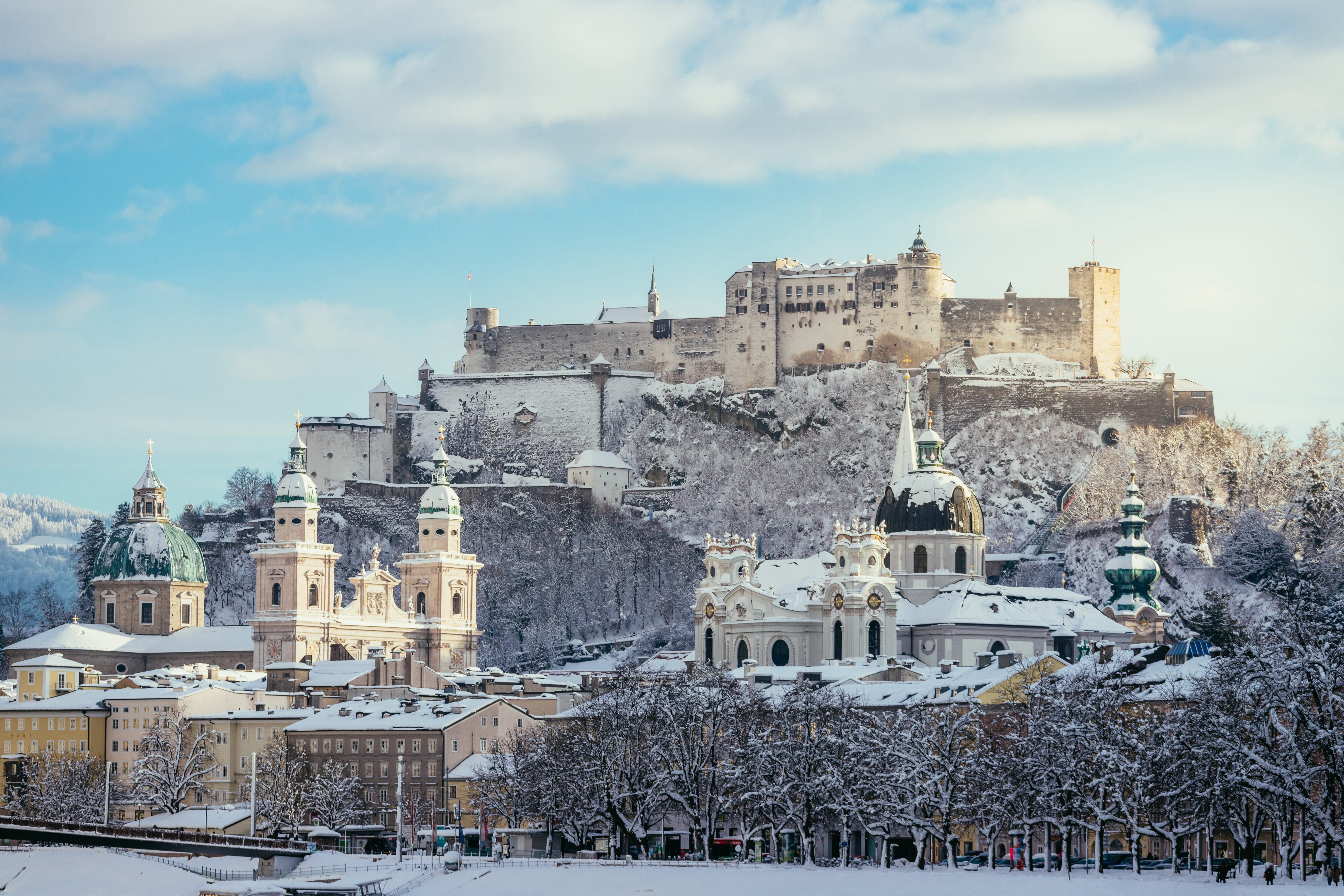 Travel to Salzburg for 22 500 Avios. In the picture, view of the Hohensalzburg Fortress, on a hill, with snow-covered roofs.