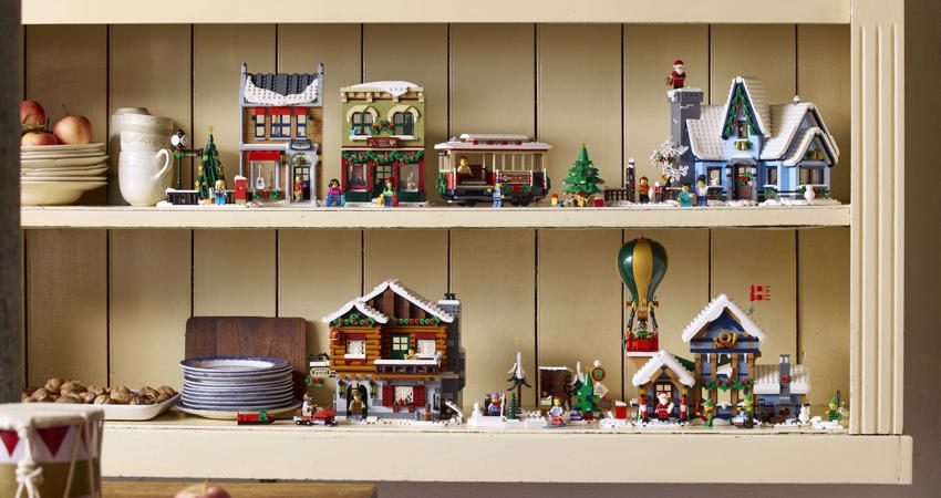 Get up to 10 Avios for every £1 you spend with Lego. Pictured here, Lego constructions from the Christmas collection on a wooden shelf, surrounded b Christmas-themed cups and dishes, with freshly baked apples and biscuits. 