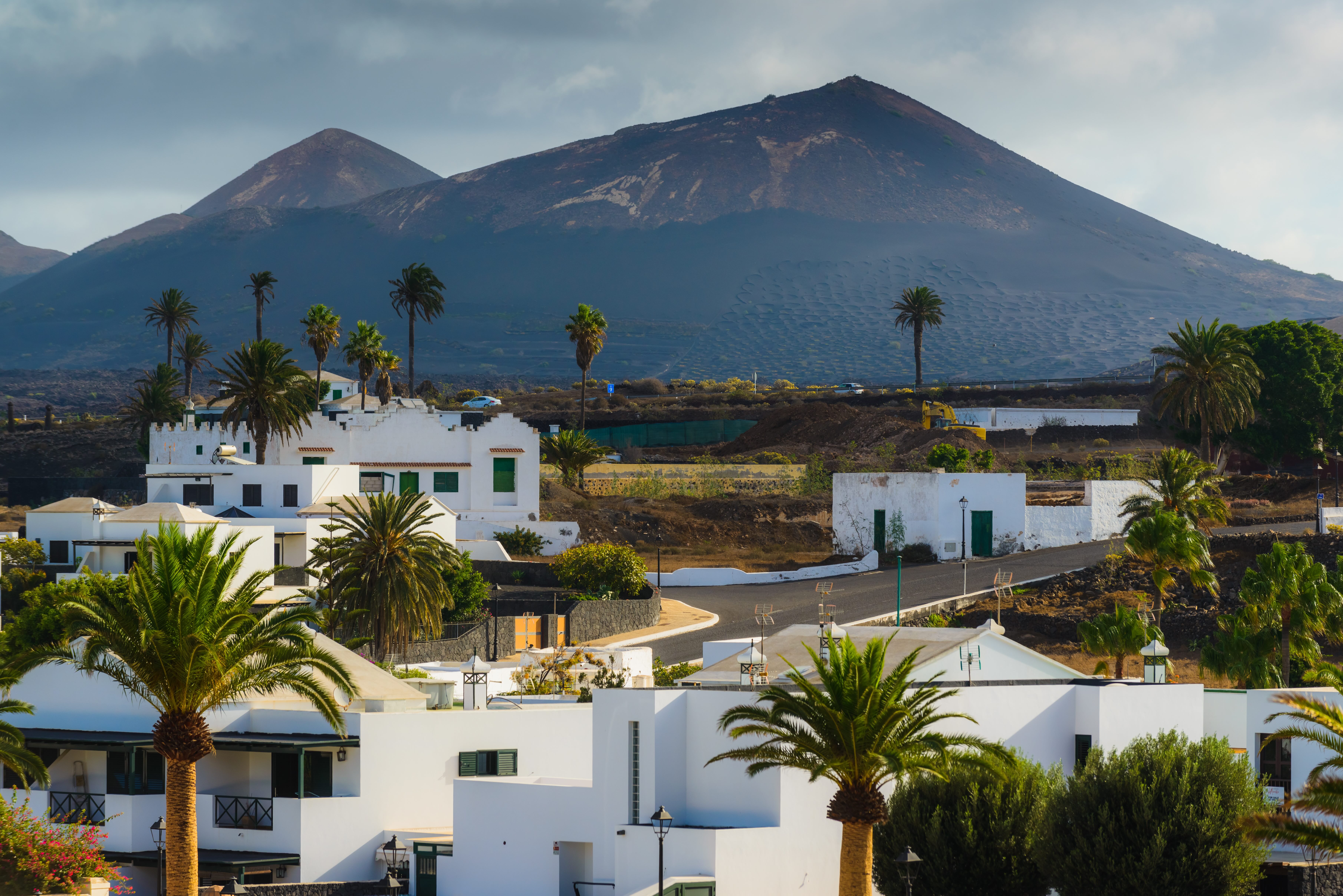 En la image, el pueblo de Yaiza en primer plano, con casitas bajas encaladas, enmarcado por el perfil de uno de los volcanes de la isla.