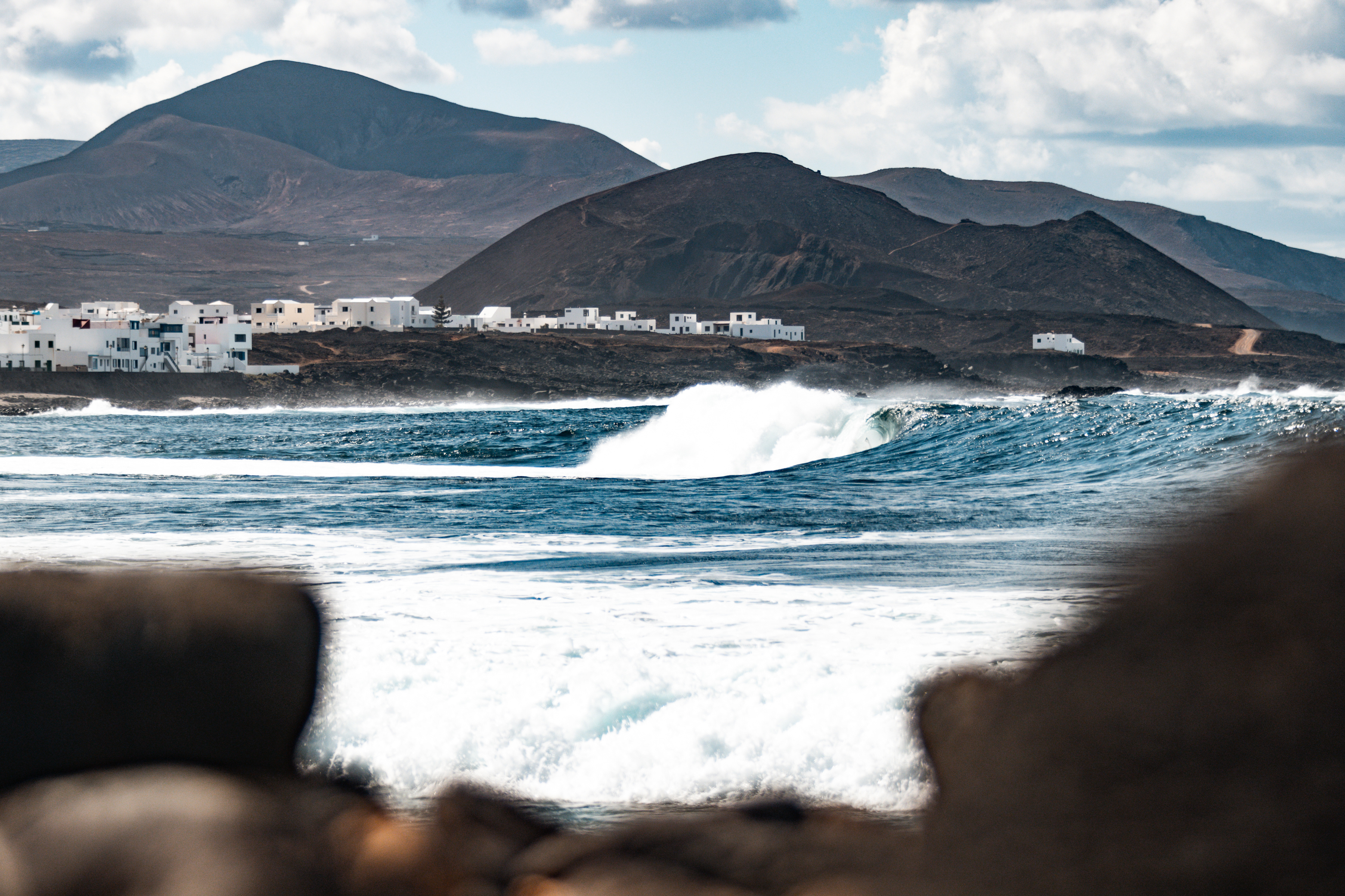En la imagen, el perfil de La Santa de fondo, sobre un paisaje lunar. En primer plano, las olas de un bar embravecido, perfecto para el surf 