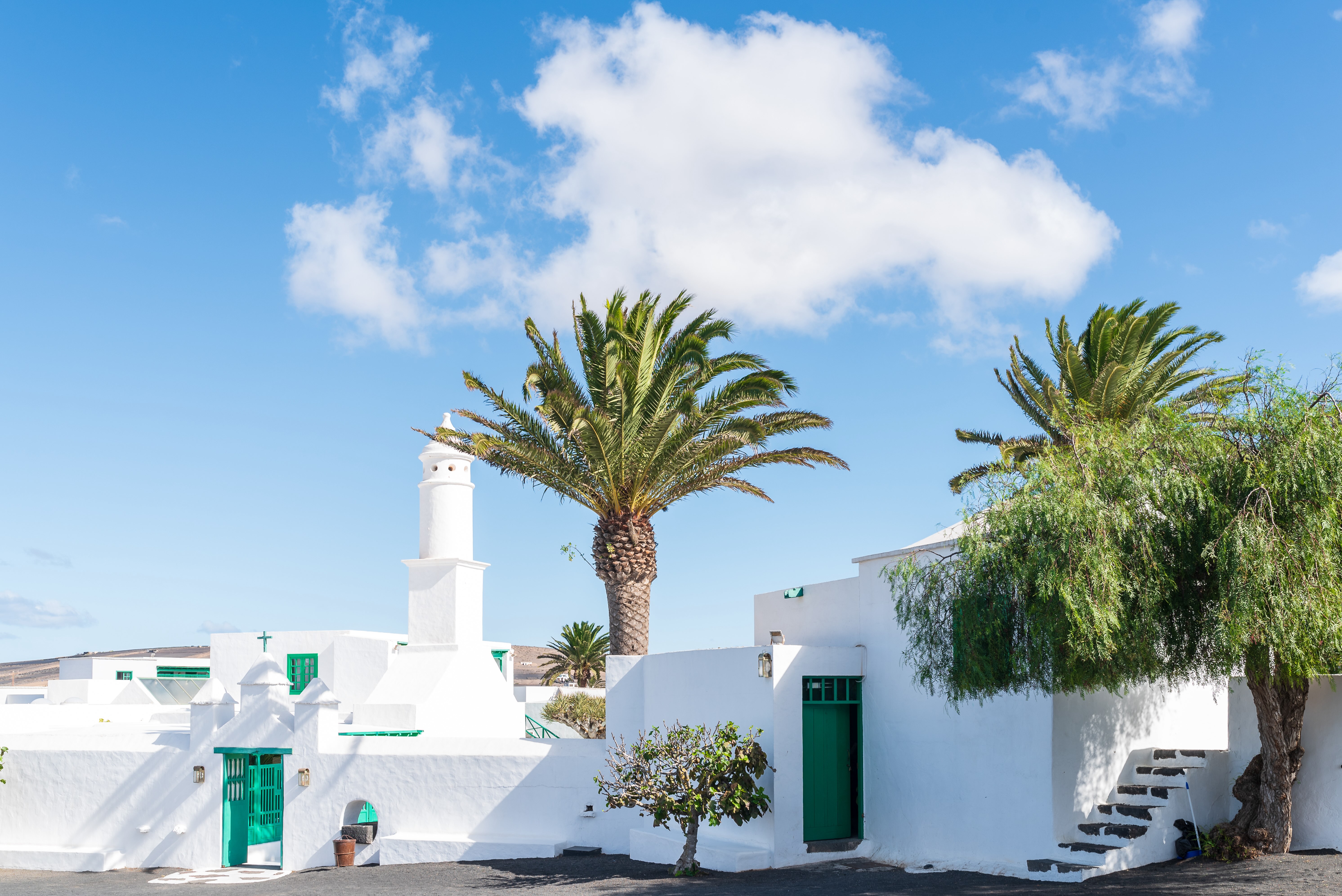 In the picture, one of the squares of San Bartolomé, with low houses dotted with palm trees. In the background is the profile of César Manrique's Monument to Fertility
