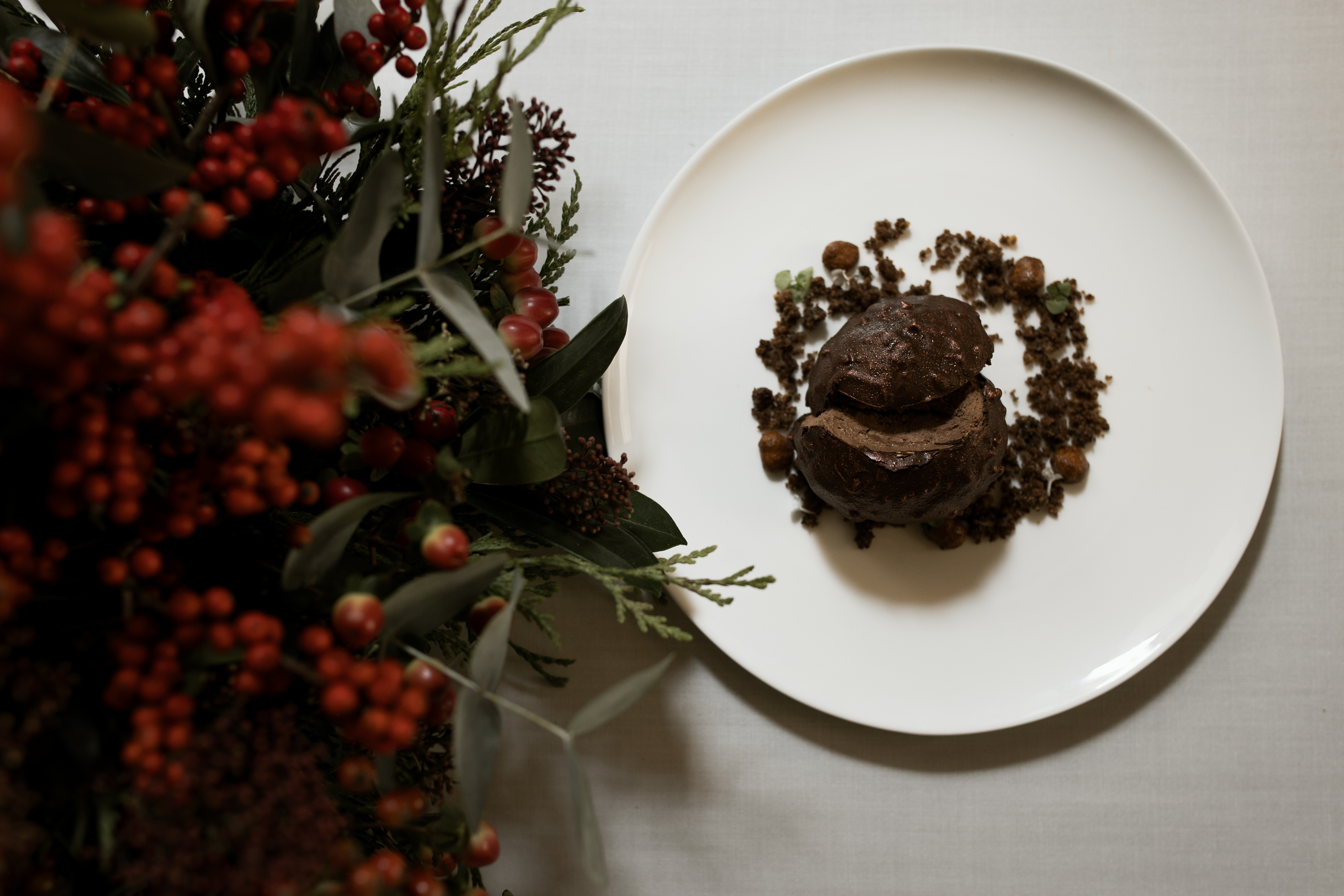 Uno de los platos de Haroma, en tonos marrones sobre un amplio plato blanco de fondo plano, junto a un centro de mesa de acebo