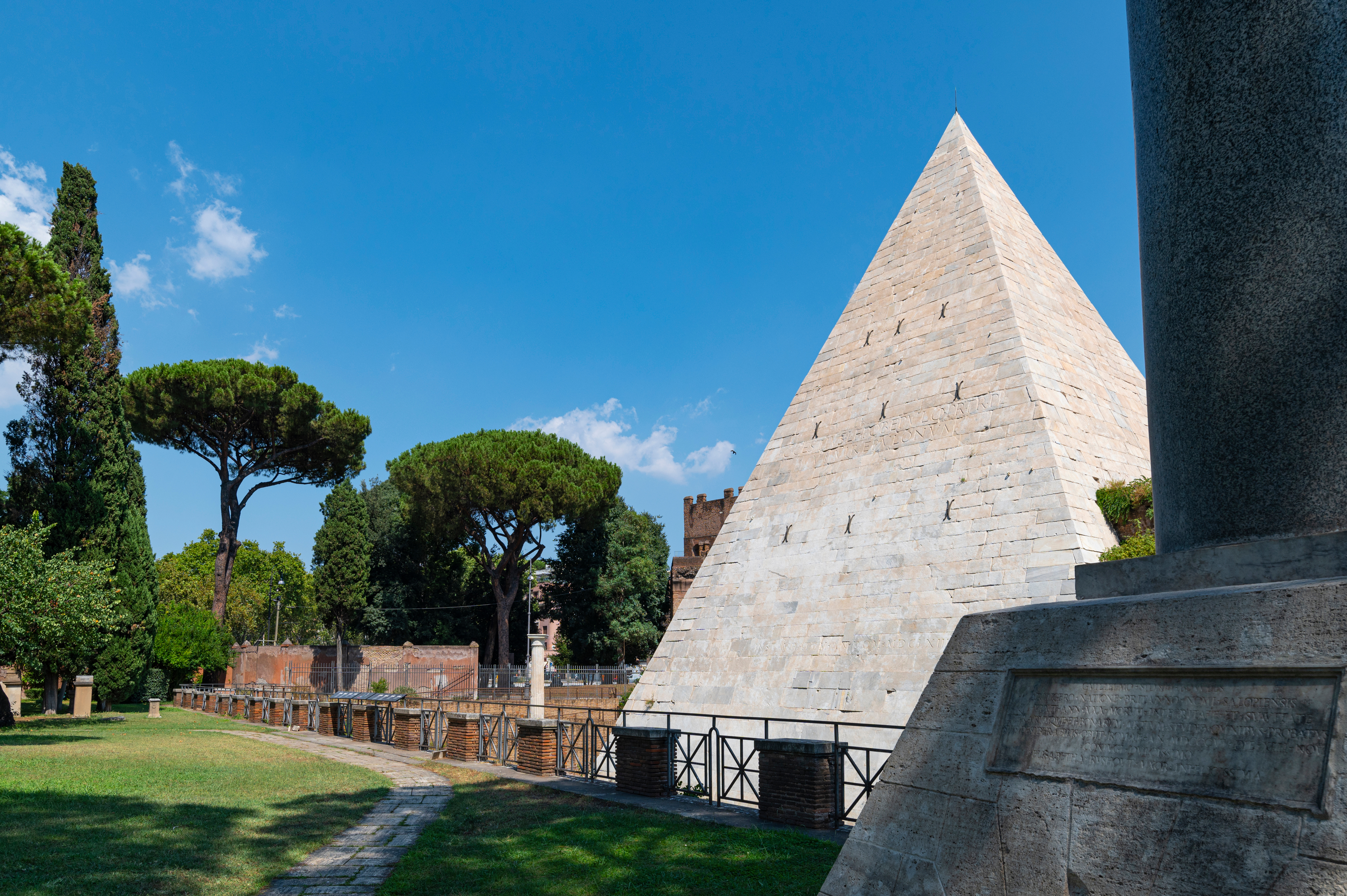 Side view of the Cestia Pyramid, with trees in the background and a blue sky.