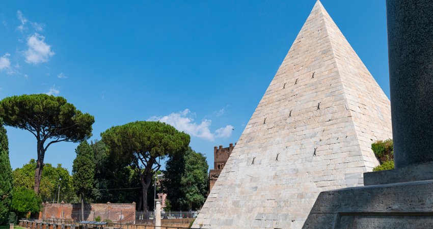 Side view of the Cestia Pyramid, with trees in the background and a blue sky.