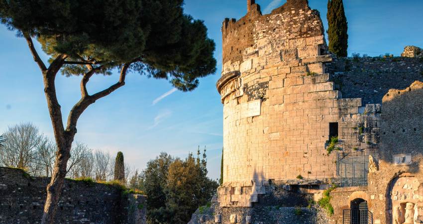 The Mausoleum of Cecilia Metella at sunset, with the circular structure and remains of the medieval wall, surrounded by trees