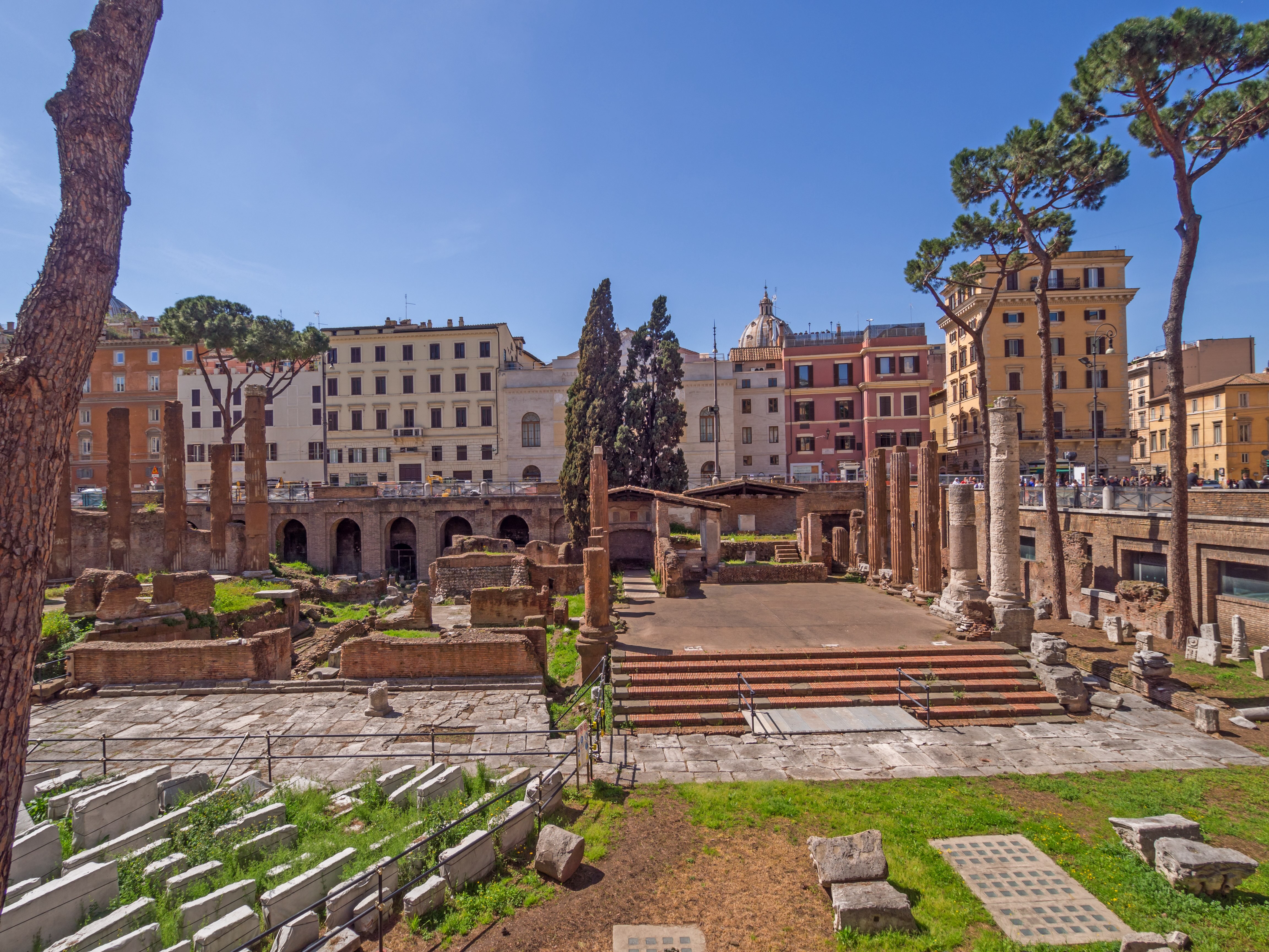 In the picture, Largo di Torre Argentina, with the steps where Caesar was assassinated on the right side of the panorama and columns, arcades and vegetation on the left side. Rome's buildings frame the landscape