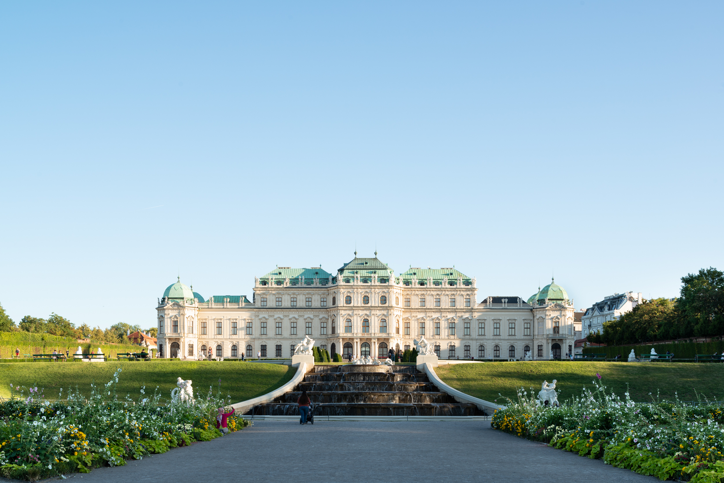 Getaway to Vienna. Back view of the Belvedere Palace at sunset in spring. The image shows part of the Baroque garden, with immaculate lawns and a gravel path flanked by flower beds