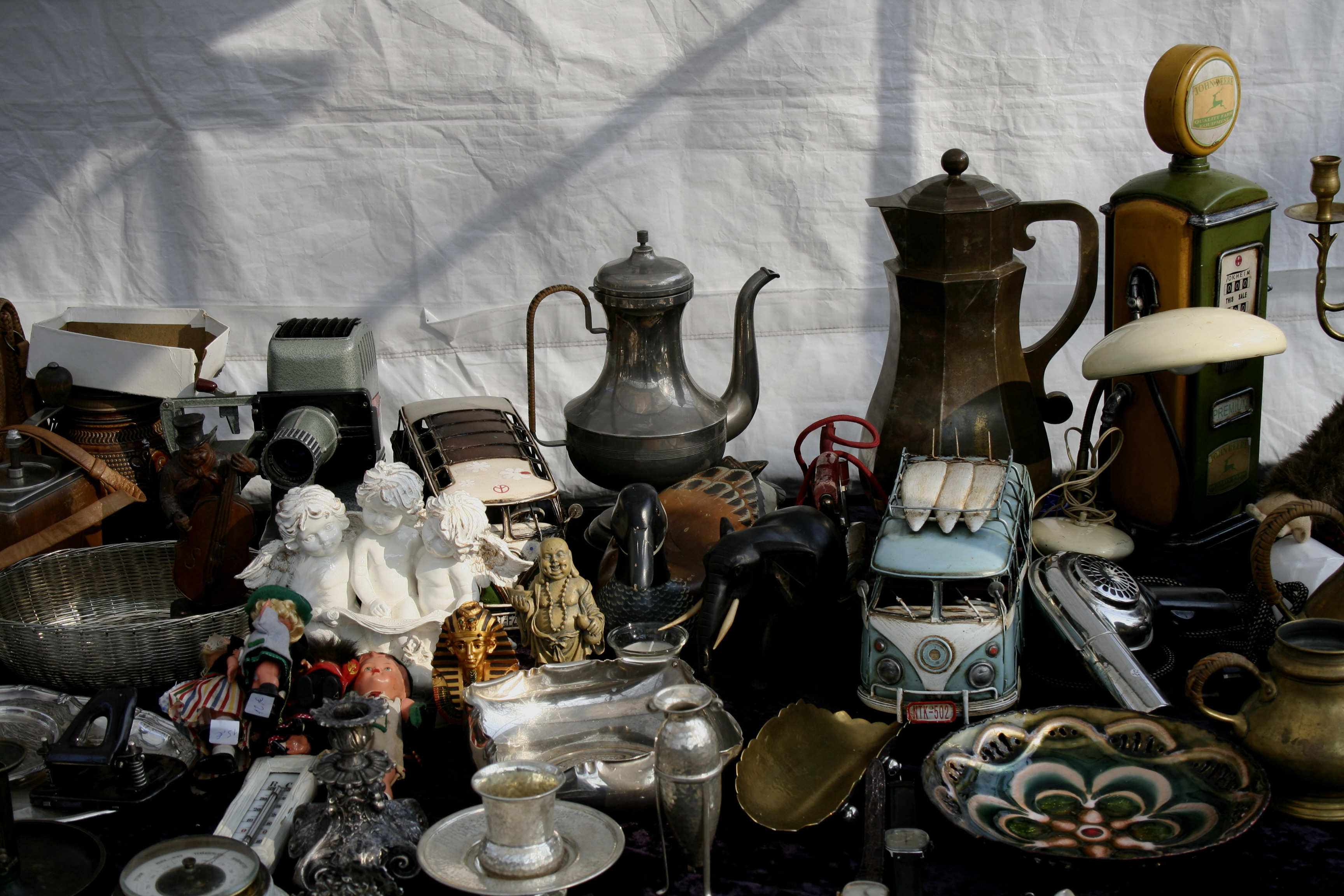In the image, one of the stalls displays a picture with a classic still life composition. Two silver teapots, a small bust of Tutankhamun, an old camera and a miniature Mercedes van