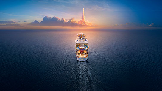 The image shows the rear of a Royal Caribbean cruise ship sailing across the sea. On the horizon, the clouds shape the Eiffel Tower.