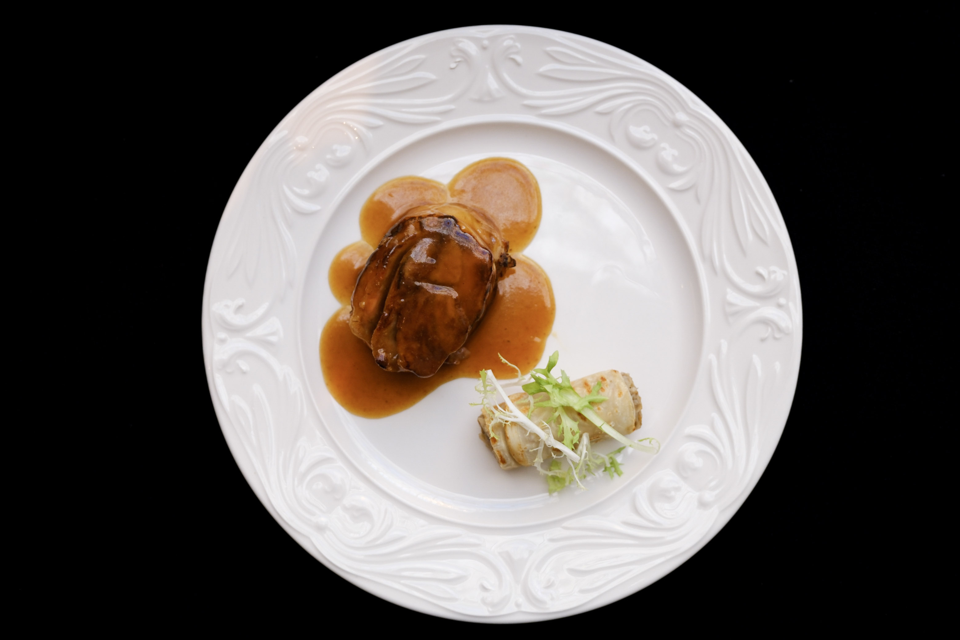 In the image, one of the porcelain plates from the Palace Hotel, on a black background. Sirloin steak in sauce with vegetable side dish.
