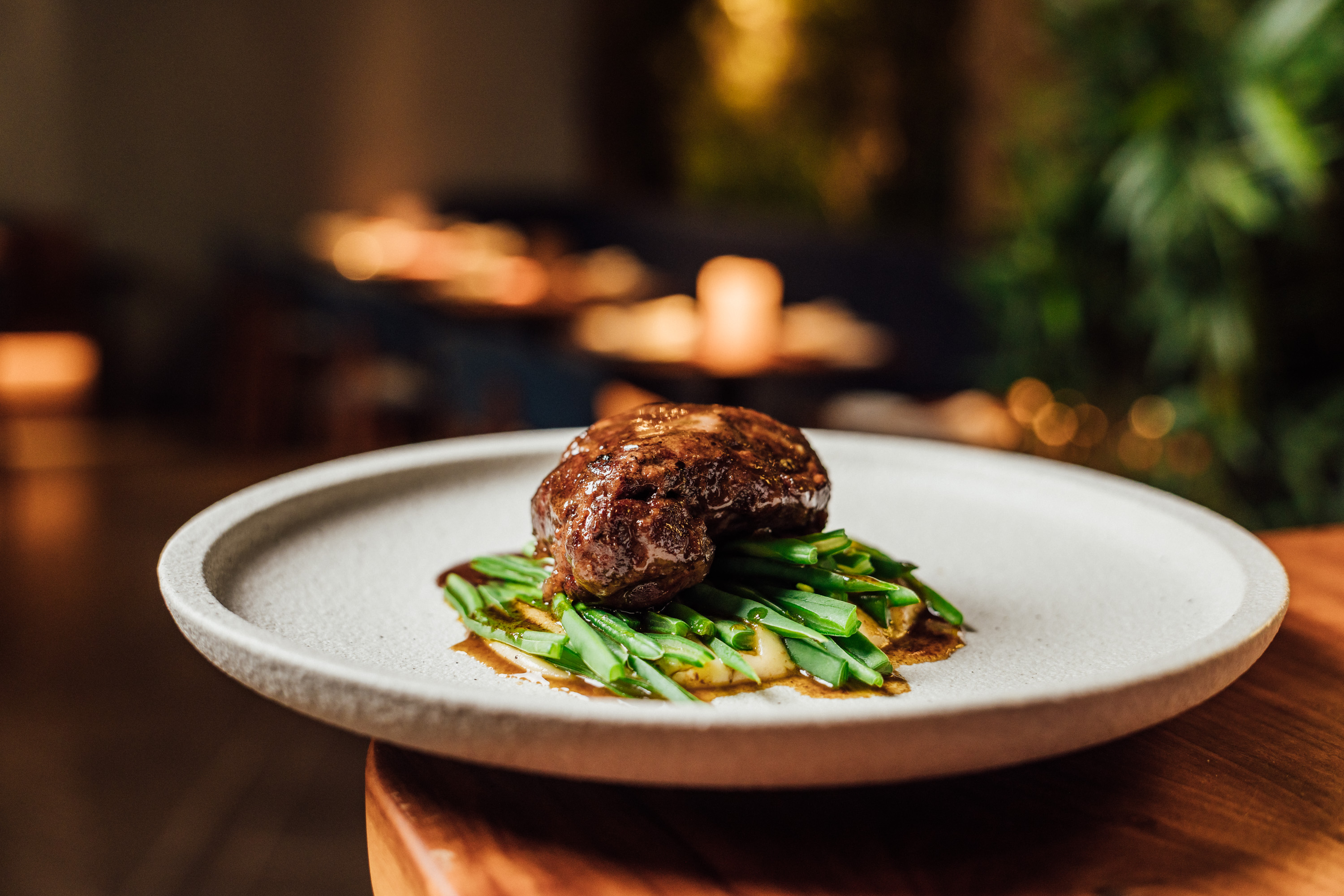 In the image, pork cheeks on a bed of vegetables in a grey ceramic dish, against a background decorated with Christmas candles