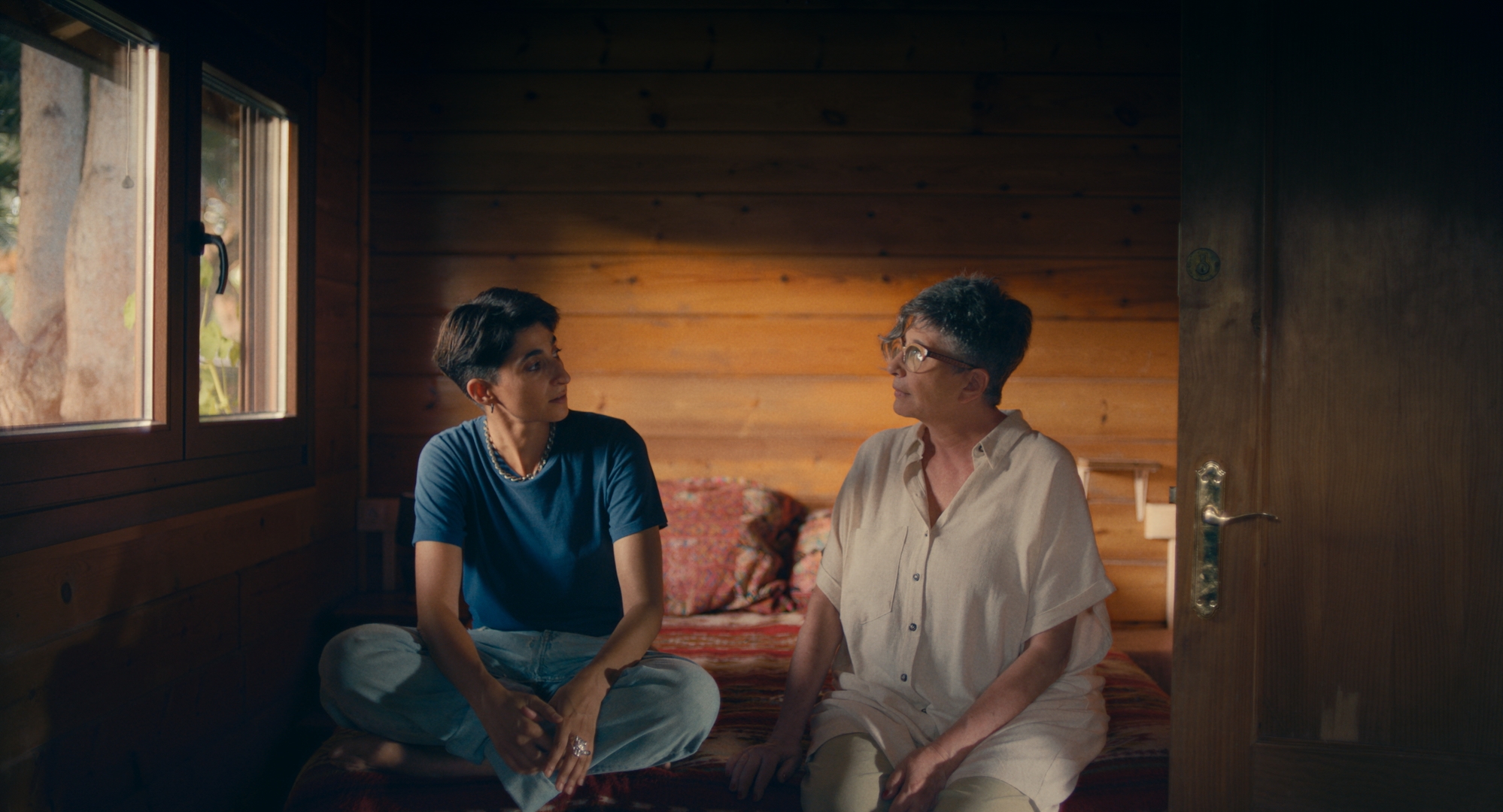 En la imagen Alba y su madre, Ana Villa, conversan sentadas al los píes de la cama en una cabaña de madera