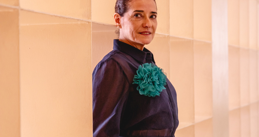 Taiyana Pimentel posa, ligeramente de perfil, en el Museo Marco, junto una pared de cubos que dejan pasar la luz. La direcotra lleva una camisa azul marino y un broche en forma de flor, hecha en gasa y de color aguamarina